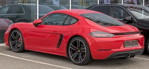 A red Porsche 718 Cayman S photographed in profile, from the four-cylinder generation that revived the 718 name.