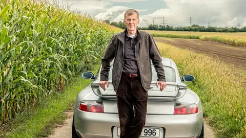 Walter Röhrl standing behind a silver 996-generation Porsche 911 GT3 with the number plate 996, the car he lapped the Nürburgring Nordschleife in under eight minutes for the first time