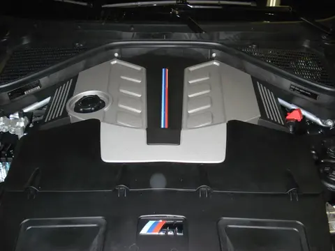 The twin-turbocharged S63 V8 sitting in the engine bay of a BMW X5 M, the unit built around a cross-bank pulse-tuned exhaust manifold.