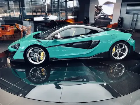 A teal McLaren 600LT in side profile on a showroom turntable with a reflective floor.