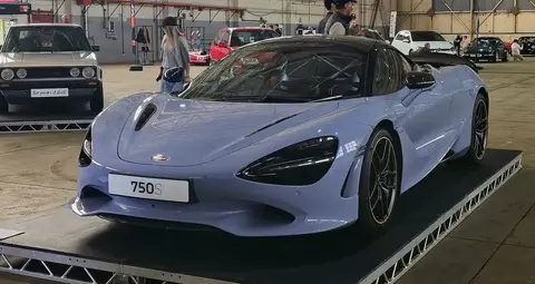A slate-blue McLaren 750S on display at a car show, its '750S' number plate visible on the front bumper.