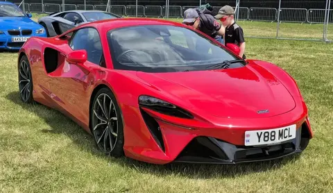 Front three-quarter view of a red McLaren Artura parked on grass at an outdoor car show.