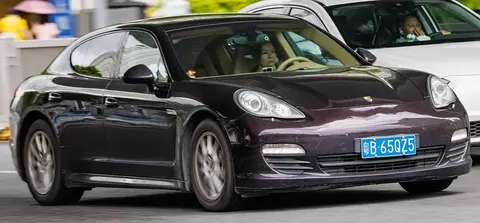 A dark purple first-generation Porsche Panamera driving through a city street with the driver visible.